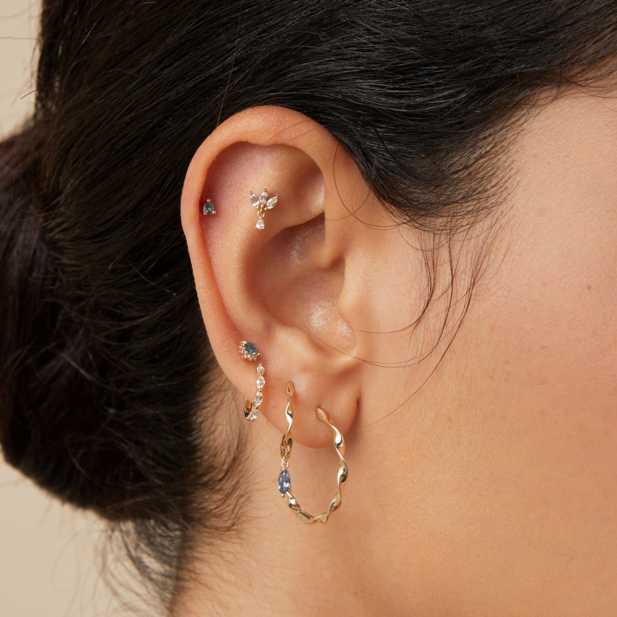 Woman wearing solid gold daith earrings stacked with other solid gold piercing jewellery on her right ear.