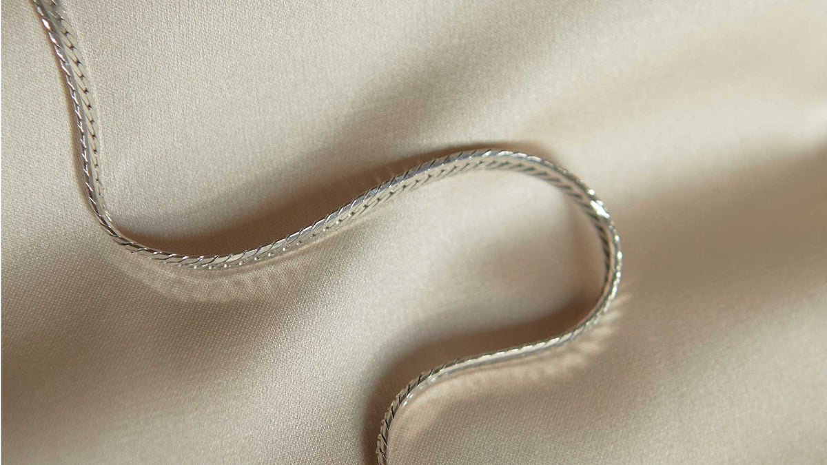 A silver snake chain necklace from Astrid & Miyu's silver plated jewellery collection elegantly displayed on beige cloth.
