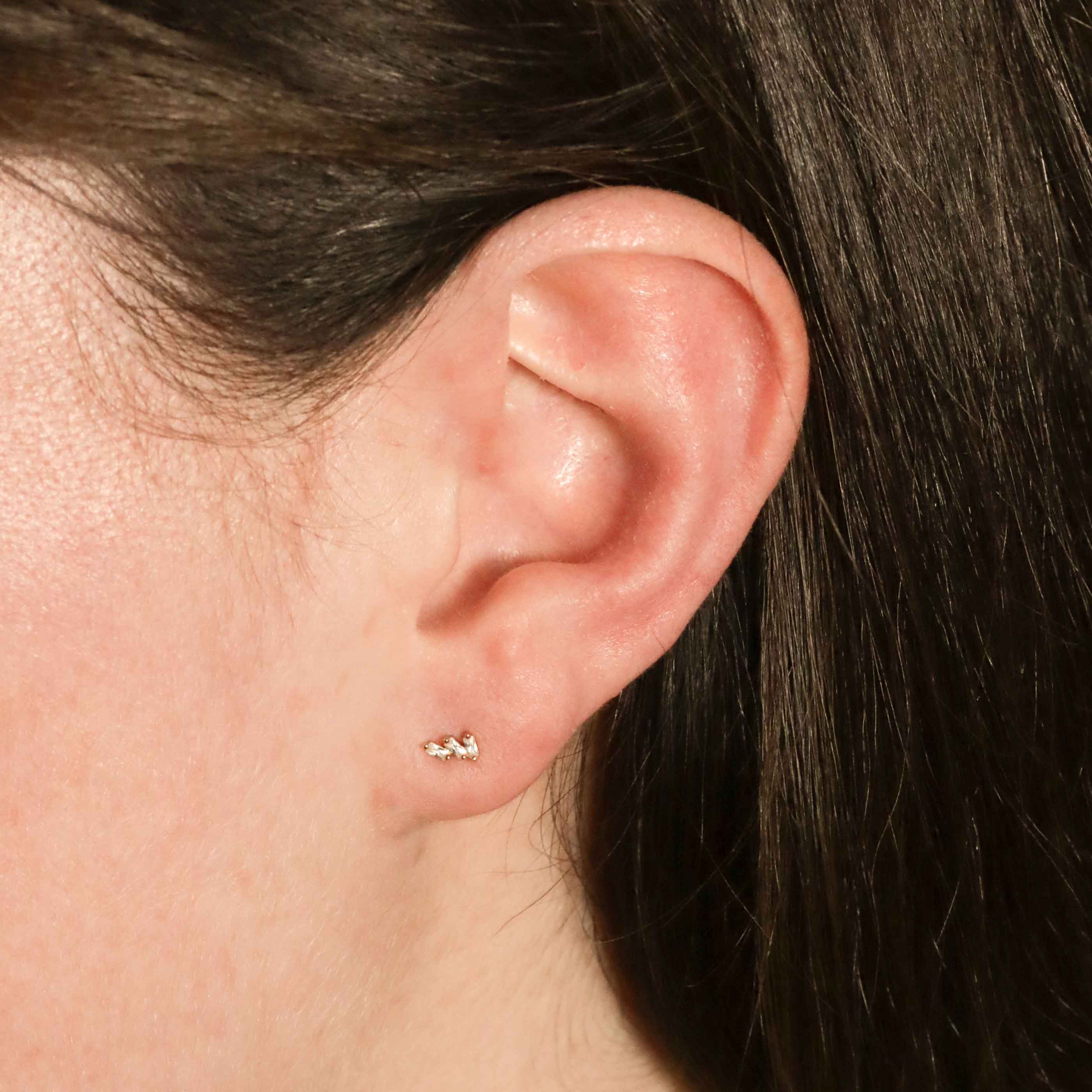 Woman wearing dainty cubic zirconia baguette studs in gold from Astrid & Miyu on her left ear.